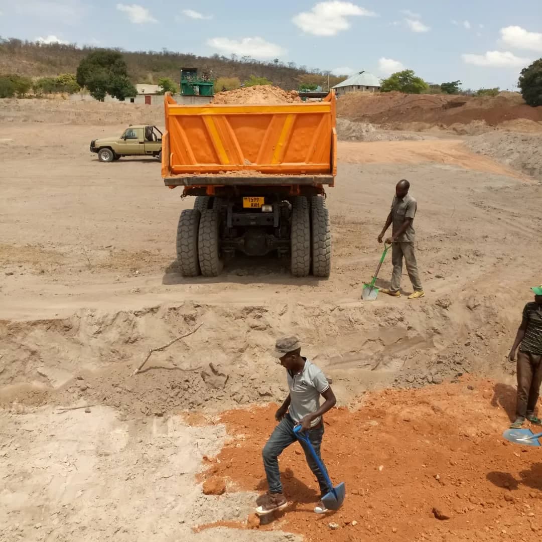 Dump truck unloading as workers level the fill by hand