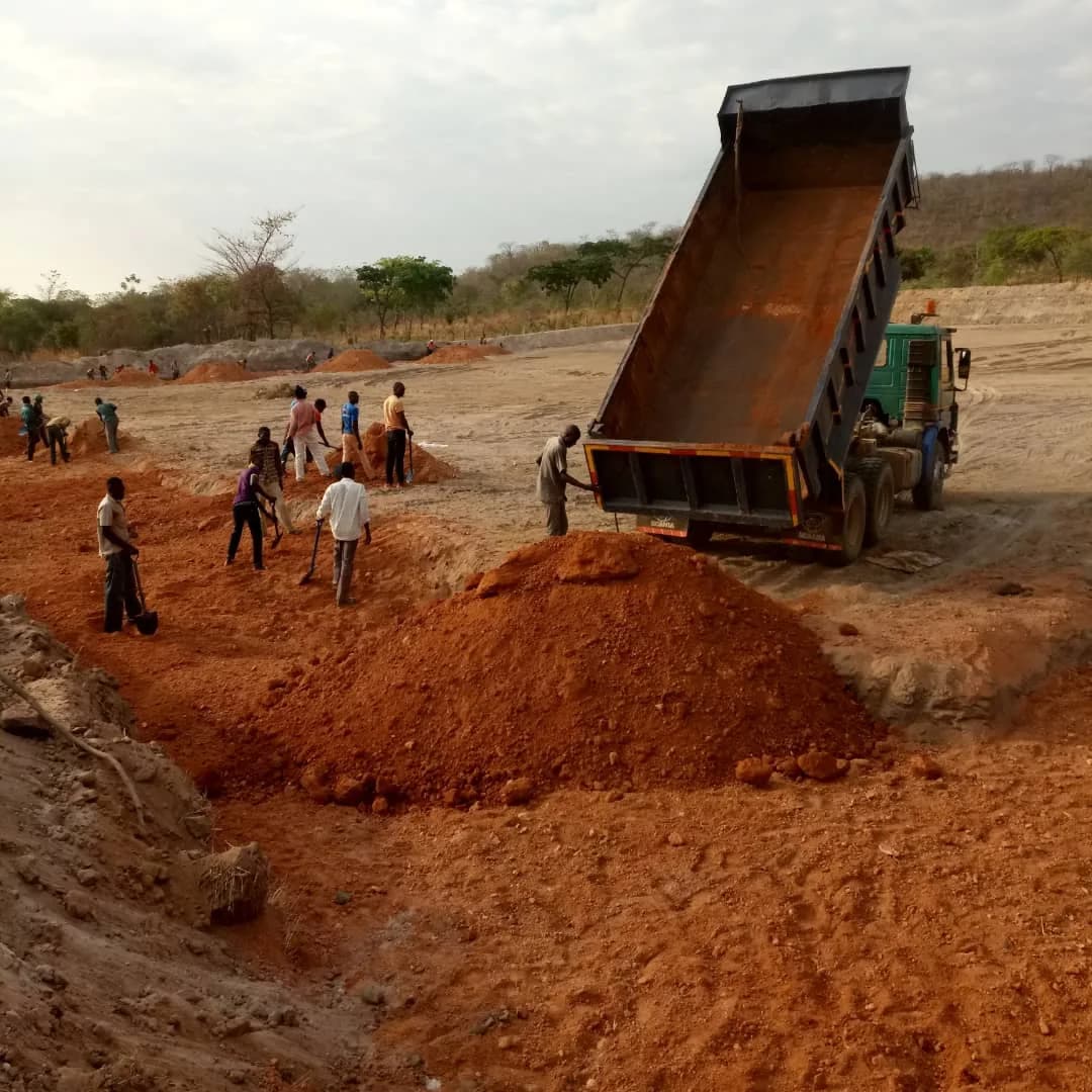 Dump truck tipping earth as workers spread it by shovel
