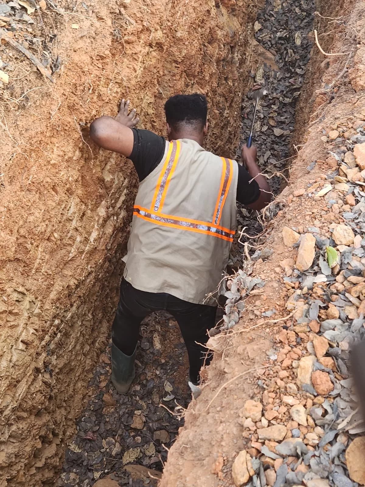 Geologist sampling rock with a hammer inside an exploration trench