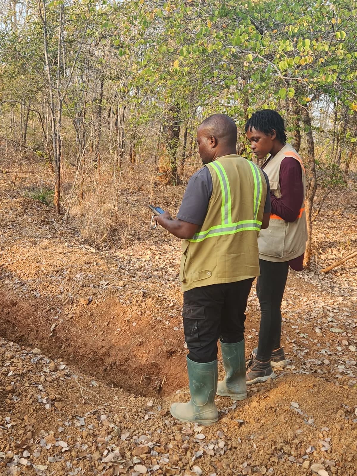 Geologists recording a GPS reading beside the trench