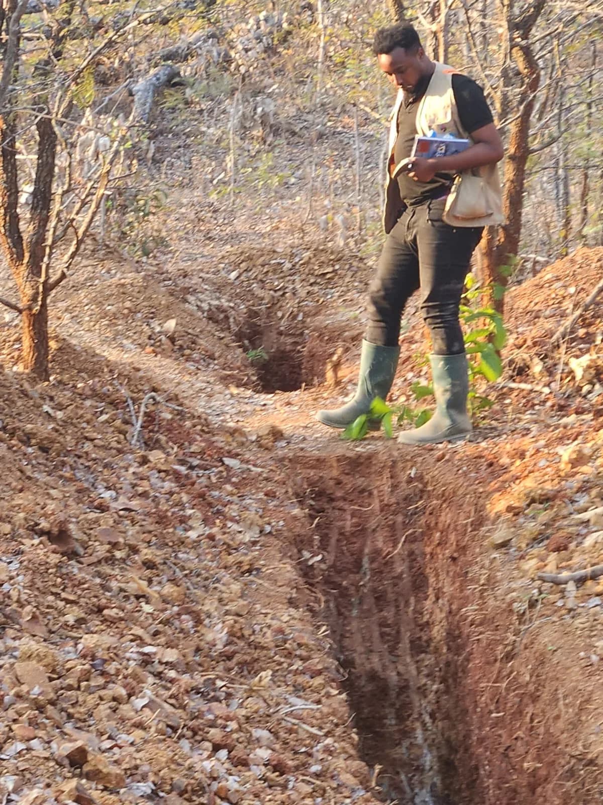 Geologist walking the trench edge carrying sample bags